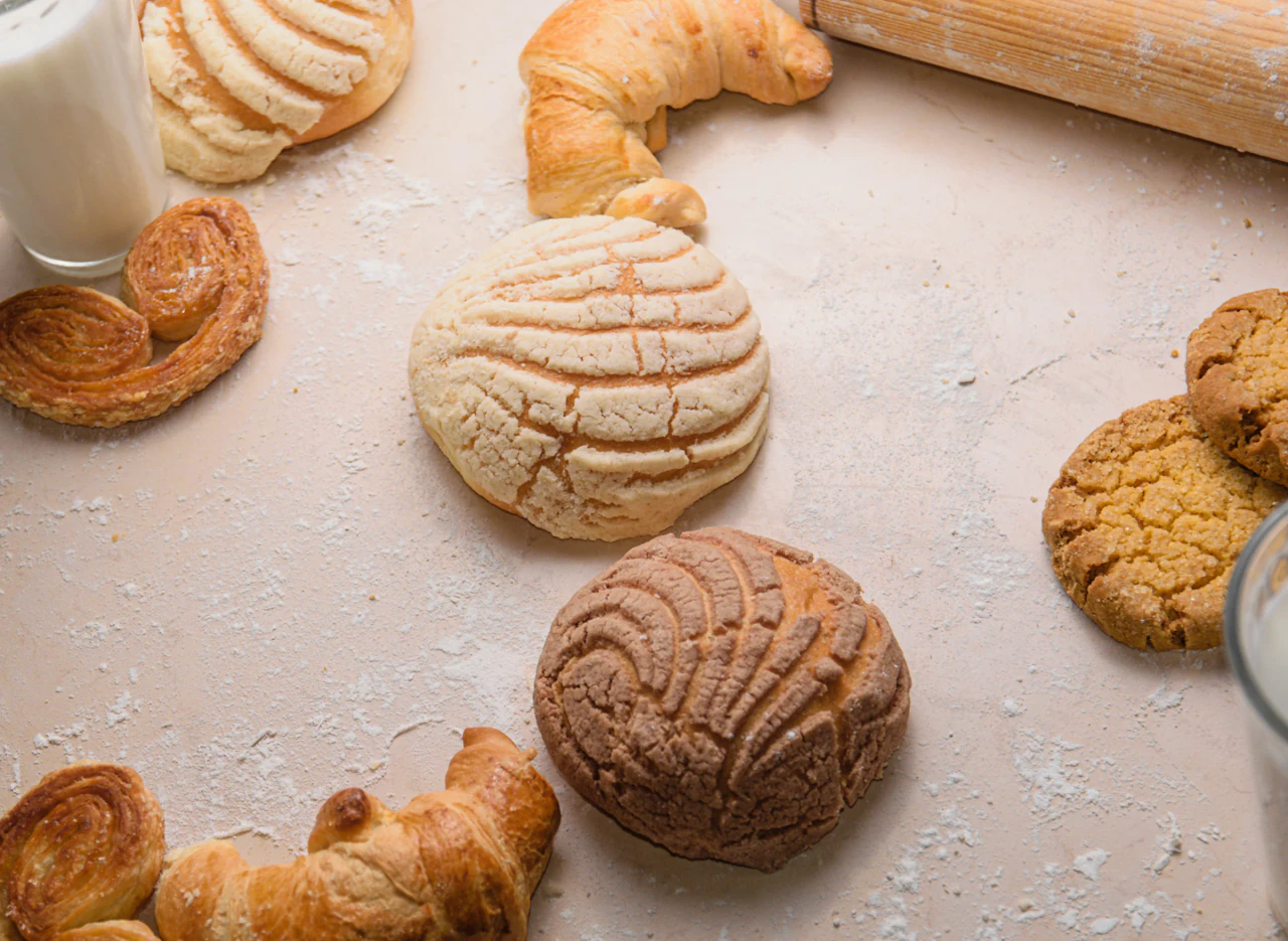 Conchas, croissants y palmeras de panadería vistos desde arriba con un vaso de leche y un rodillo