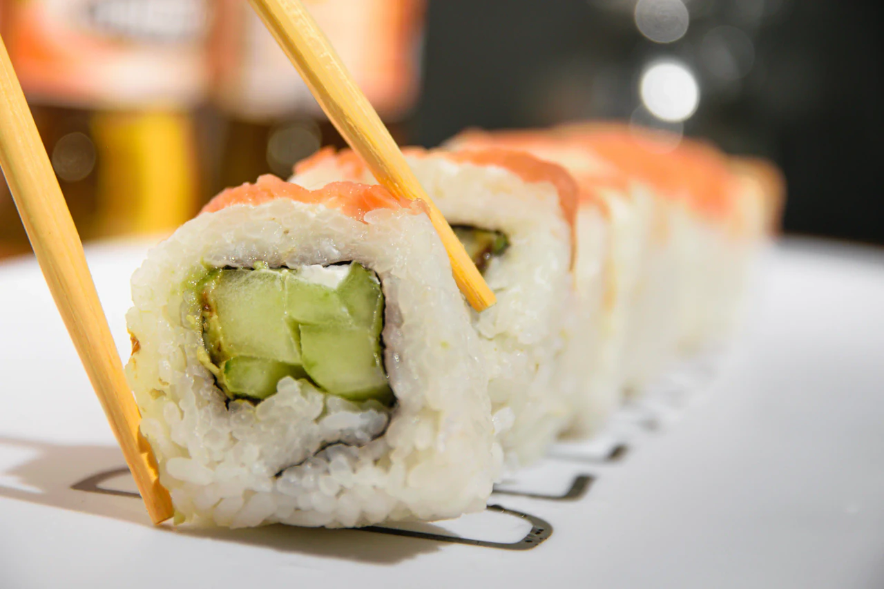 Rollo de sushi levantado con palillos sobre una fila de piezas