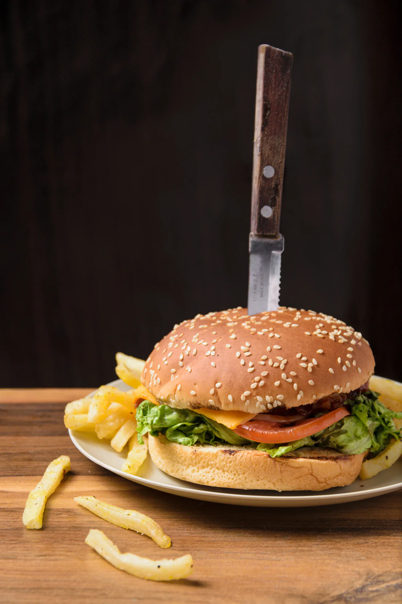 Hamburguesa con papas fritas y cuchillo clavado, fotografiada sobre mesa de madera